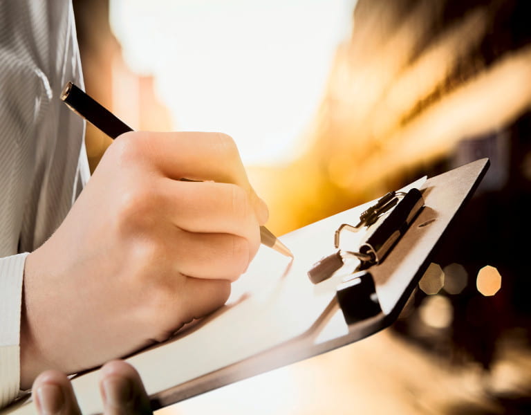 Hand schreibt mit Stift auf Klemmbrett im Sonnenlicht