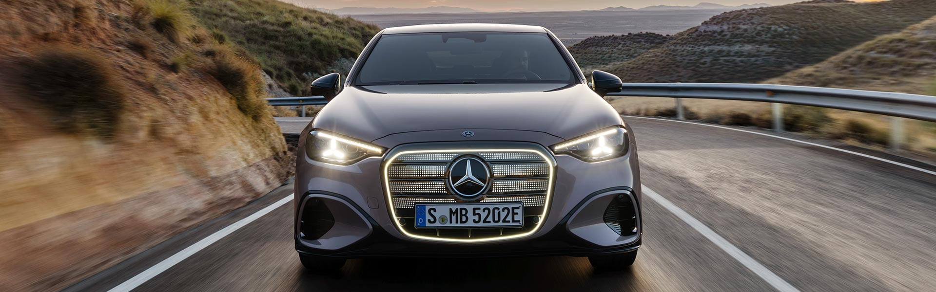 graue Mercedes-Benz C-Klasse Limousine in der Frontansicht mit beleuchtetem Kühlergrill während der Fahrt