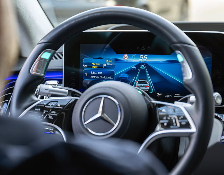 Blick über die Schulter des Fahrers auf das Lenkrad und den Tacho der Mercedes-Benz S-Klasse mit aktiviertem MB Drive Pilot