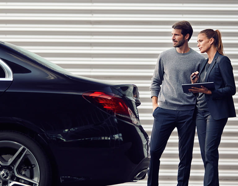 Mann und Frau stehen am Heck eines schwarzen Mercedes-Benz