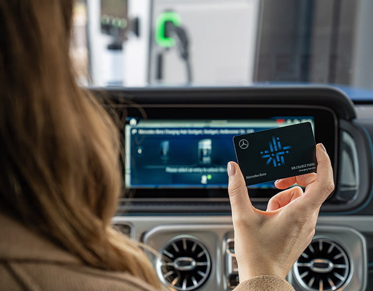 Frau hält Mercedes-Benz Charge Public Karte vor das Infotainmentsystem ihren Fahrzeugs