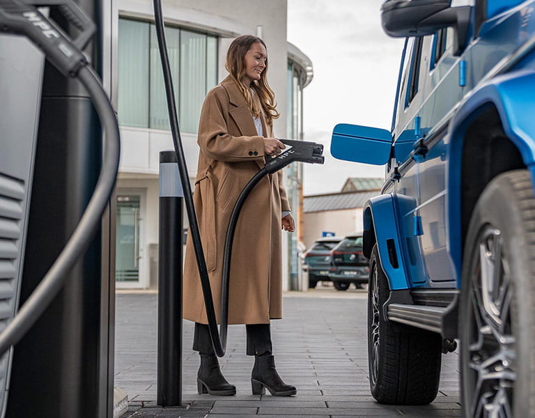 Frau steckt ihren voll elektrischen Mercedes-Benz an die Ladestation