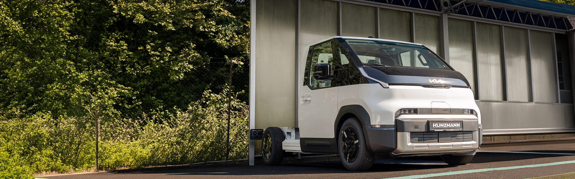 Kia PV5 Chassis Cab Pritsche in der 3/4 Frontansicht unter einem Carport Kia PV5 Chassis Cab Pritsche in der 3/4 Frontansicht unter einem Carport