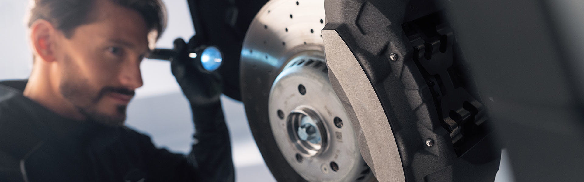Mechatroniker mit Taschenlampe beim Kontrollieren der Bremsen eines Fahrzeugs