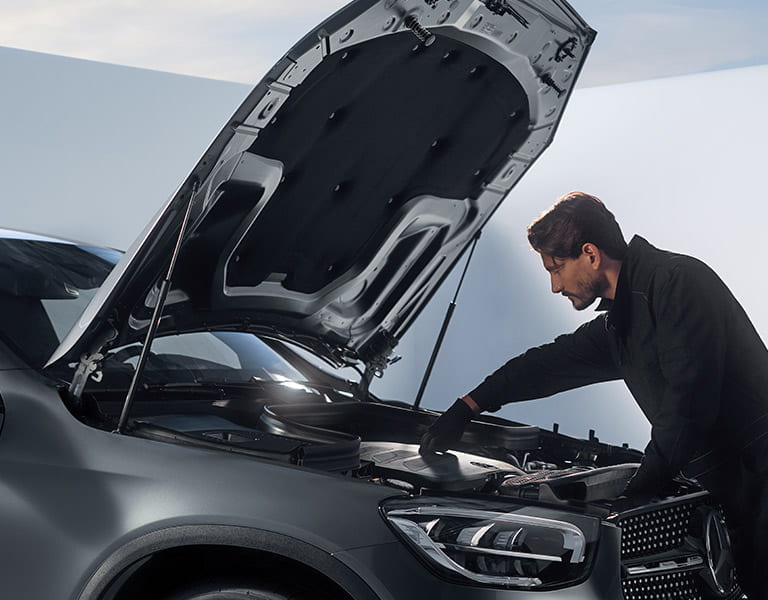 Kfz Mechatroniker vor offener Motorhaube am Fahrzeug