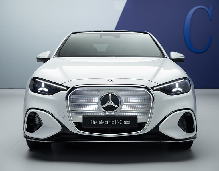 Die reinelektrische Mercedes-Benz C-Klasse in weiß mit beleuchtetem in der Frontansicht