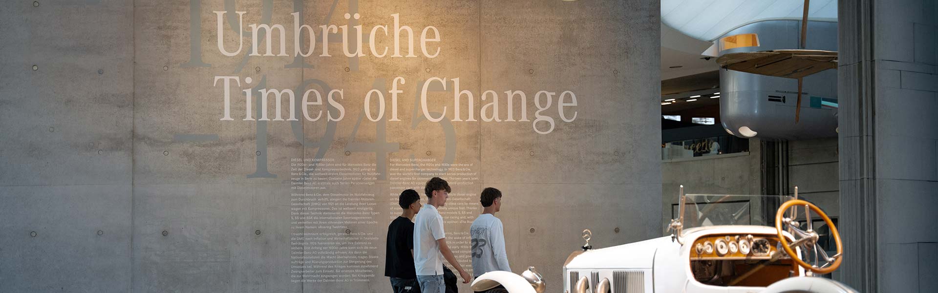 Drei Kunzmann Azubis im Mercedes-Benz Museum vor der Wand "Times of Change" mit einem Oldtimer im Vordergrund