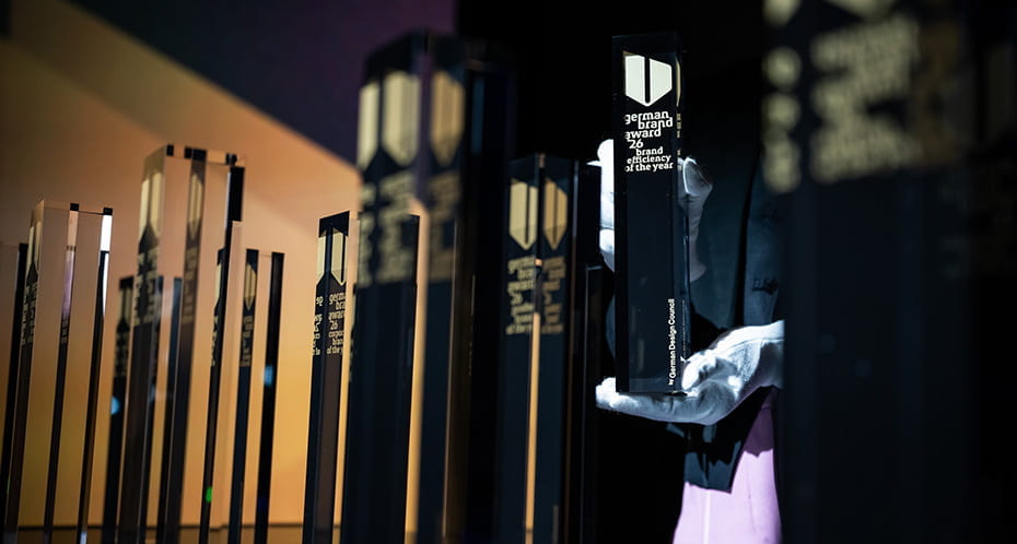 Pokale des German Brand Award platziert durch mit Samthandschuhen geschützten Händen