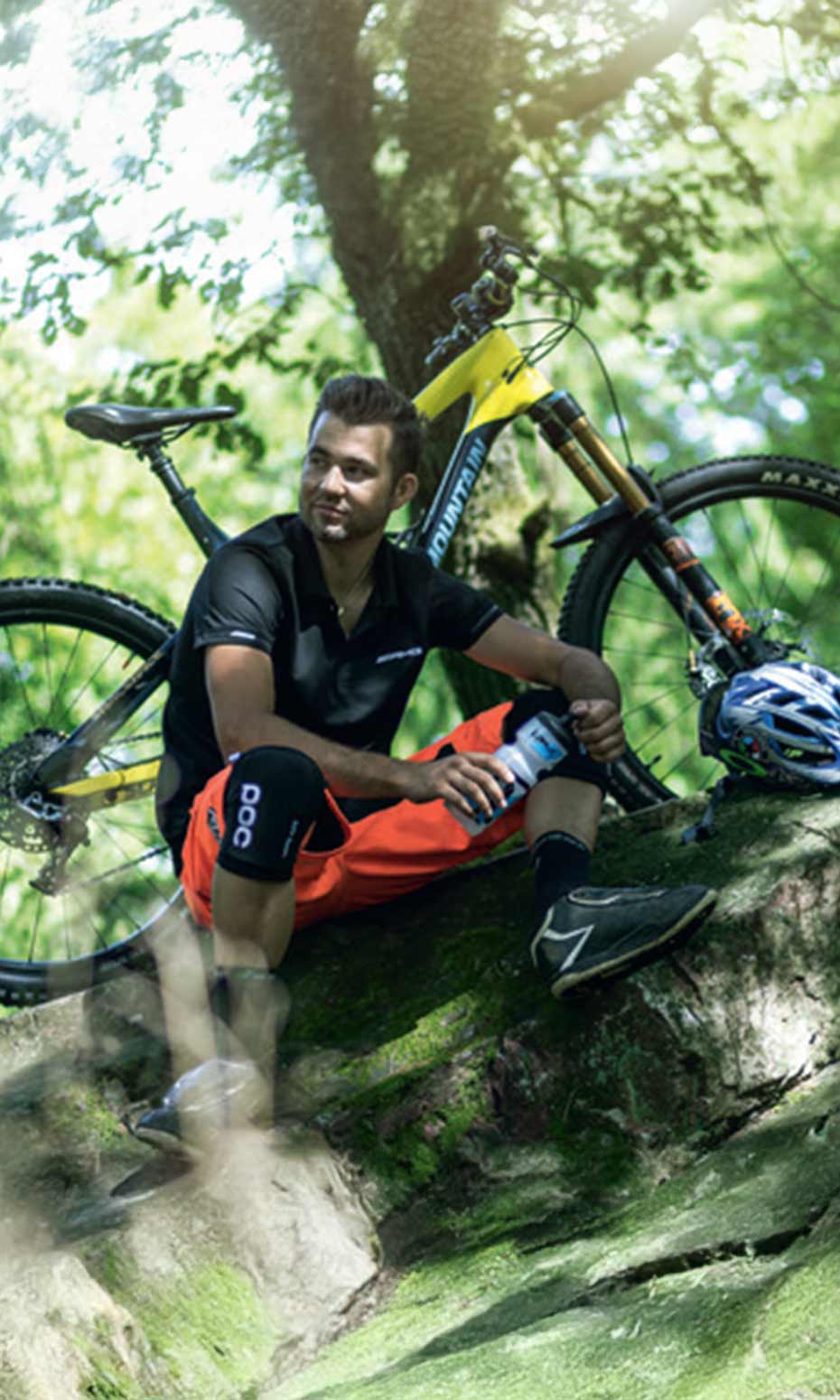 Pascal Stenger beim Pause machen auf einem Stein im Wald. im Hintergrund steht sein Mountainbike Pascal Stenger beim Pause machen auf einem Stein im Wald. im Hintergrund steht sein Mountainbike